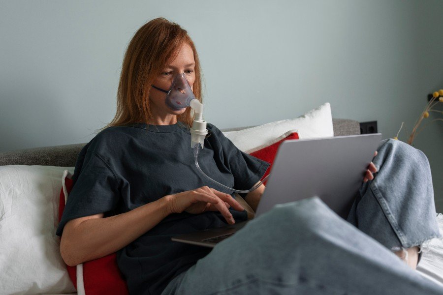 Woman using an Oxygen Concentrator mask while working on a laptop at home.