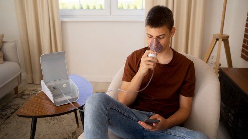 Teen boy using a Sleep Apnea Machine at home while sitting in a comfortable chair and holding a smartphone